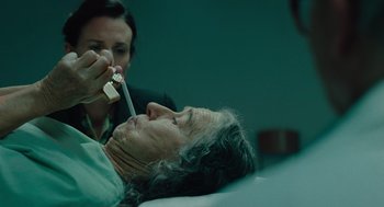 Movie still from “Golda” (2023), directed by Guy Nattiv – An older woman laying in a hospital bed while a nurse looks on; Close Up shot, Over the shoulder angle
