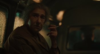 Movie still from “Golda” (2023), directed by Guy Nattiv – An older man smoking a cigarette in a dark room; Close Up shot, Over the shoulder angle