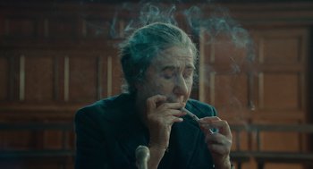 Movie still from “Golda” (2023), directed by Guy Nattiv – An older woman smoking a cigarette while sitting at a table; Close Up shot, Over the shoulder angle