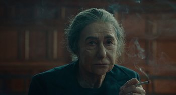 Movie still from “Golda” (2023), directed by Guy Nattiv – An older woman smoking a cigarette in a dark room; Close Up shot, Over the shoulder angle
