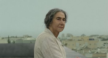 Movie still from “Golda” (2023), directed by Guy Nattiv – An older woman standing on top of a building; Close Up shot, Over the shoulder angle
