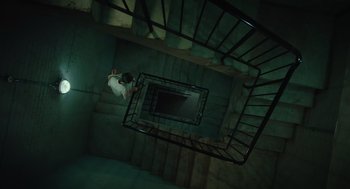 Movie still from “Golda” (2023), directed by Guy Nattiv – A man is climbing down a spiral staircase; Wide shot, Overhead angle