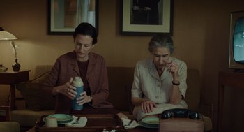 Movie still from “Golda” (2023), directed by Guy Nattiv – Two women are sitting at a table and one is holding a drink; Medium shot, High angle