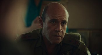 Movie still from “Golda” (2023), directed by Guy Nattiv – A man with a bald head wearing a military uniform; Close Up shot, Over the shoulder angle