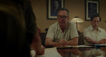 Movie still from “Golda” (2023), directed by Guy Nattiv – A man sitting at a table with papers in front of him; Medium shot, Over the shoulder angle