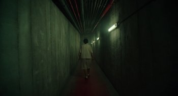 Movie still from “Golda” (2023), directed by Guy Nattiv – A woman walking down a dark hallway in a building; Extreme Wide shot, High angle