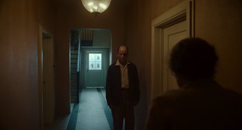 Movie still from “Golda” (2023), directed by Guy Nattiv – A man standing in a hallway next to an older woman; Wide shot, Low angle