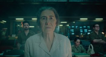 Movie still from “Golda” (2023), directed by Guy Nattiv – An older woman is standing in front of a group of people; Close Up shot, Low angle