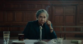 Movie still from “Golda” (2023), directed by Guy Nattiv – An older woman sitting at a table smoking a cigarette; Medium shot, Over the shoulder angle