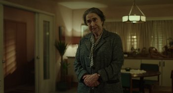 Movie still from “Golda” (2023), directed by Guy Nattiv – An older woman standing in a living room with her arms crossed; Medium shot, Over the shoulder angle