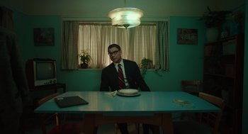 Movie still from “Golda” (2023), directed by Guy Nattiv – A man sitting at a table with a plate in front of him; Wide shot, Low angle