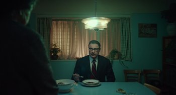 Movie still from “Golda” (2023), directed by Guy Nattiv – A man sitting at a dinner table with a plate of food; Medium shot, Low angle