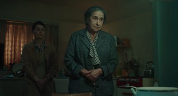 Movie still from “Golda” (2023), directed by Guy Nattiv – An older woman standing in a room next to another woman; Medium shot, Over the shoulder angle