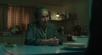 Movie still from “Golda” (2023), directed by Guy Nattiv – An older woman sitting at a table in a kitchen; Medium shot, Over the shoulder angle