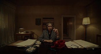 Movie still from “Golda” (2023), directed by Guy Nattiv – An older woman sitting at a table in a dark room; Medium shot, High angle