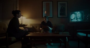 Movie still from “Golda” (2023), directed by Guy Nattiv – An older man sitting on a couch in a living room; Wide shot, Over the shoulder angle