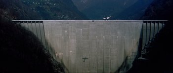 Movie still from “GoldenEye” (1995), directed by Martin Campbell – A plane is flying over a large concrete wall; Extreme Wide shot, High angle