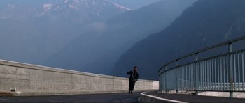 Movie still from “GoldenEye” (1995), directed by Martin Campbell – A man walking on the side of a road near a mountain; Extreme Wide shot, High angle