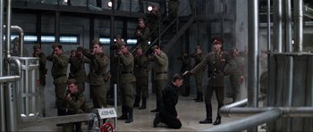 Movie still from “GoldenEye” (1995), directed by Martin Campbell – A man kneeling down in front of a group of men in uniform; Wide shot, High angle