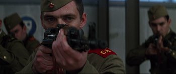 Movie still from “GoldenEye” (1995), directed by Martin Campbell – A man in uniform holding a rifle and aiming it; Close Up shot, Low angle