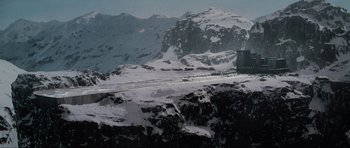 Movie still from “GoldenEye” (1995), directed by Martin Campbell – A truck driving down a snow covered road next to a mountain range; Extreme Wide shot, High angle