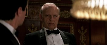 Movie still from “GoldenEye” (1995), directed by Martin Campbell – An older man wearing a tuxedo and a bow tie; Close Up shot, Low angle