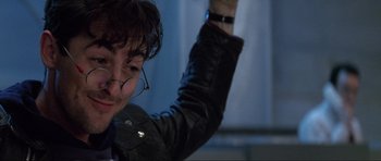 Movie still from “GoldenEye” (1995), directed by Martin Campbell – A man with glasses and a leather jacket holding his arm up in the air; Close Up shot, Low angle