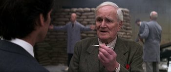 Movie still from “GoldenEye” (1995), directed by Martin Campbell – An older man holding a cigarette in his mouth; Close Up shot, Over the shoulder angle