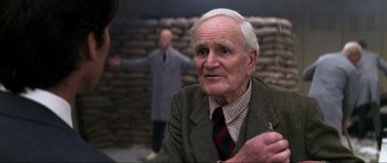 Movie still from “GoldenEye” (1995), directed by Martin Campbell – An older man wearing a suit and tie; Close Up shot, Over the shoulder angle