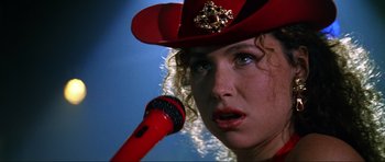 Movie still from “GoldenEye” (1995), directed by Martin Campbell – A person holding a microphone up to their mouth; Close Up shot, Over the shoulder angle