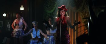 Movie still from “GoldenEye” (1995), directed by Martin Campbell – A woman in a red hat sings into a microphone; Medium shot, Over the shoulder angle