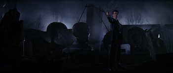 Movie still from “GoldenEye” (1995), directed by Martin Campbell – A man in a suit and tie holding up a gun; Wide shot, Low angle