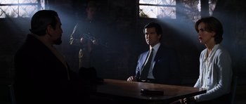 Movie still from “GoldenEye” (1995), directed by Martin Campbell – A man sitting at a table in a dark room; Medium shot, Over the shoulder angle