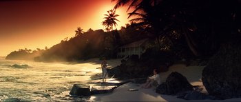 Movie still from “GoldenEye” (1995), directed by Martin Campbell – Two people are sitting on the beach at sunset; Extreme Wide shot, High angle