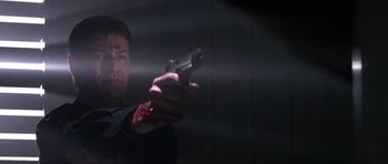 Movie still from “GoldenEye” (1995), directed by Martin Campbell – A man holding a gun with blood on his face; Close Up shot, Low angle