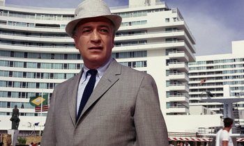 Movie still from “Goldfinger” (1964), directed by Guy Hamilton – A man in a suit and hat standing in front of a building; Medium shot, Low angle