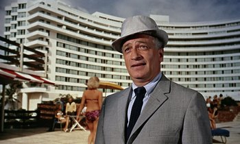 Movie still from “Goldfinger” (1964), directed by Guy Hamilton – A man wearing a suit and a hat standing in front of a hotel; Medium shot, Low angle