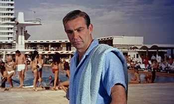 Movie still from “Goldfinger” (1964), directed by Guy Hamilton – A man with a towel around his neck standing on the beach; Medium shot, Low angle