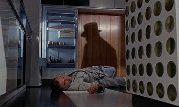Movie still from “Goldfinger” (1964), directed by Guy Hamilton – A man laying on the ground in a kitchen; Wide shot, Low angle
