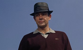 Movie still from “Goldfinger” (1964), directed by Guy Hamilton – A man wearing a black hat and a maroon sweater; Close Up shot, Low angle