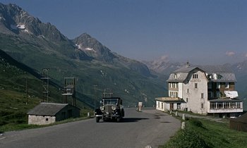 Movie still from “Goldfinger” (1964), directed by Guy Hamilton – An old car driving down a road in the mountains; Extreme Wide shot, High angle