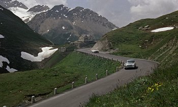 Movie still from “Goldfinger” (1964), directed by Guy Hamilton – A car driving down a road near a mountain range; Extreme Wide shot, High angle