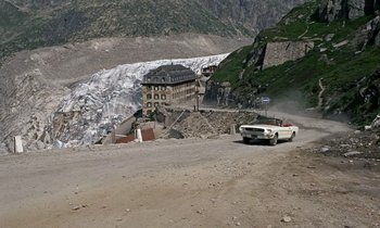 Movie still from “Goldfinger” (1964), directed by Guy Hamilton – A car driving down a road next to a mountain; Extreme Wide shot, High angle