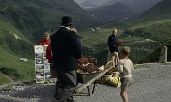 Movie still from “Goldfinger” (1964), directed by Guy Hamilton – A group of people standing on a road near mountains; Wide shot, High angle