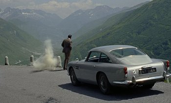 Movie still from “Goldfinger” (1964), directed by Guy Hamilton – A man walking on the side of a road next to a car; Wide shot, High angle