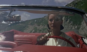 Movie still from “Goldfinger” (1964), directed by Guy Hamilton – A woman sitting in the driver's seat of a red car; Medium shot, Low angle