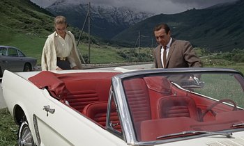 Movie still from “Goldfinger” (1964), directed by Guy Hamilton – A man and a woman standing in the back seat of a car; Wide shot, High angle