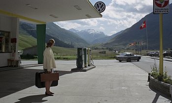 Movie still from “Goldfinger” (1964), directed by Guy Hamilton – A man holding a briefcase at a gas station with mountains in the background; Wide shot, Low angle