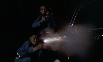 Movie still from “Goldfinger” (1964), directed by Guy Hamilton – Two men are holding guns in the dark; Medium shot, Low angle