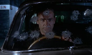 Movie still from “Goldfinger” (1964), directed by Guy Hamilton – A man driving a car with bullet holes in the windshield; Close Up shot, Over the shoulder angle